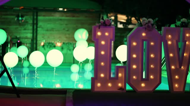 Love word neon lights, stylish evening decor for wedding ceremony glow by swimming pool at night