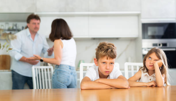 istock Two children sitting at the kitchen table sadly while their parents quarrelling 1496752461