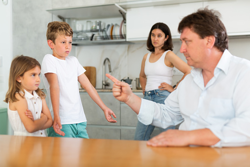 Mom and dad scold their guilty daughter and son in kitchen at home