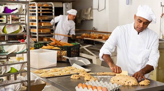 male baker in white uniform rolling out dough in kitchen
