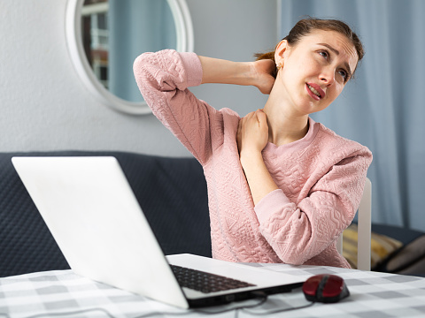 Young woman experiencing neck pain after working on laptop at home