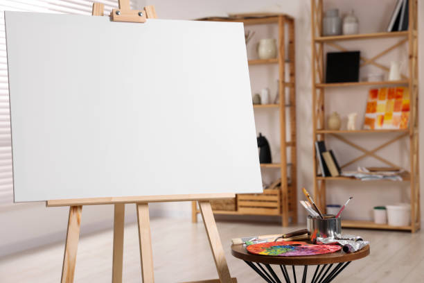 istock Wooden easel with blank canvas and different art supplies in studio, closeup 1496753991