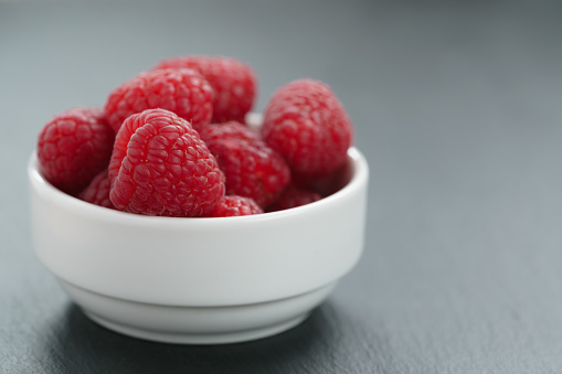 fresh raspberries in white bowl on slate board, shallow focus