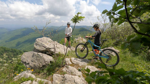 istock Mountain bikers push bike to viewpoint over valley, forest 1496755551