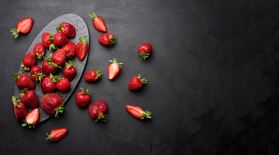 Ripe red strawberries on a black table, top view. Copy space