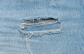 Fragment of blue jeans fabric with a hole, full frame, close up