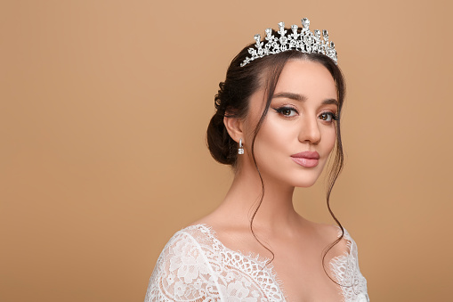 Beautiful young woman wearing luxurious tiara on beige background, space for text