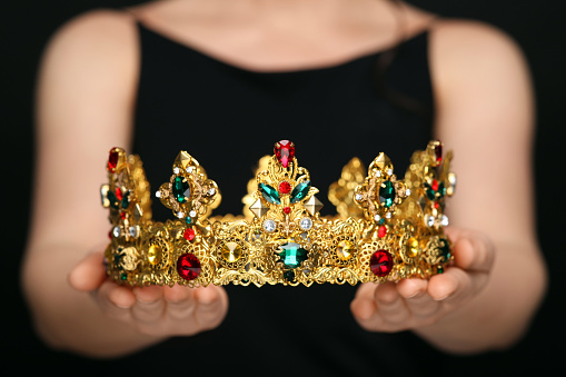 Woman holding luxurious crown on black background, closeup