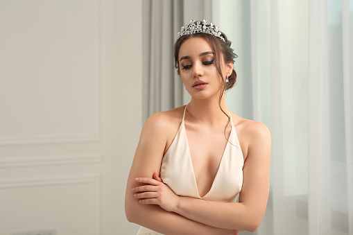 Beautiful young woman wearing luxurious tiara indoors, space for text