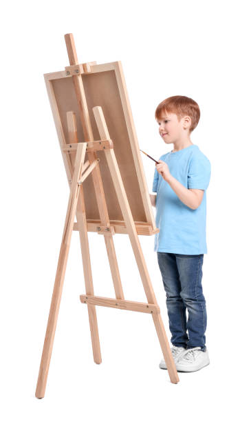 Little boy painting against white background. Using easel to hold canvas