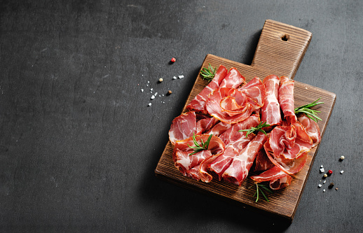 Table top shot of Mediterranean Italian foods with cold cuts meats such as salami and copocollo, along with parmesan cheese and vegetables (garlic, olives, red peppers and tomatoes).