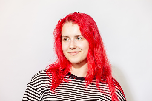Studio portrait of a young white woman with long pink hair in a striped t-shirt against a white background
