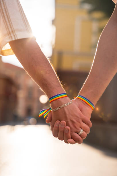 particolare della tenuta per mano di una coppia di uomini omosessuali con la bandiera arcobaleno alla festa del pride in città, concetto lgbt - gay pride wristband rainbow lgbt foto e immagini stock