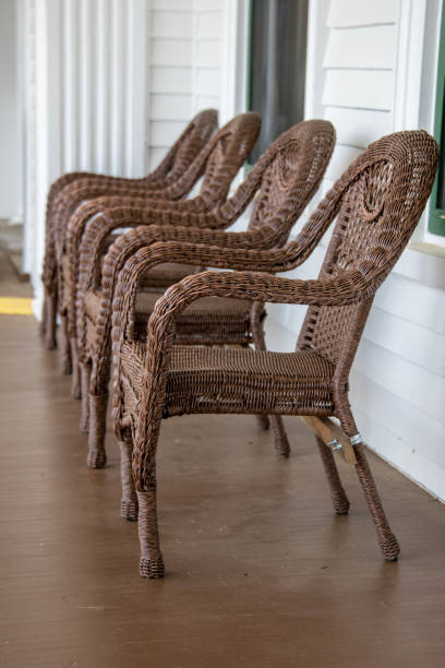 wicker chairs A row of four wicker chairs on a porch.  Brown chairs on a brown floor against a white wall. robert michaud stock pictures, royalty-free photos & images
