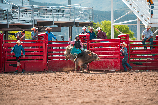 Bull riding rodeo in Utah, USA. Young cowboy riding a bull in the arena. Other cowboys looking over in the background, following the action.