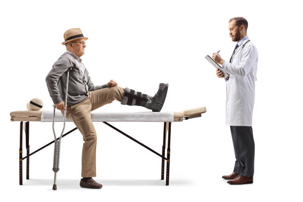 doctor writing a prescription and an elderly male patient sitting on a physical therapy bed with a brace on his leg - physical injury men orthopedic equipment isolated on white imagens e fotografias de stock