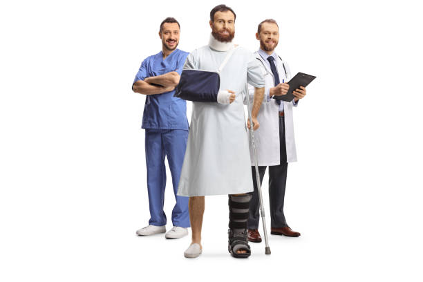 team of doctors and a male patient with an orthopedic boot and cervical collar in a hospital gown - physical injury men orthopedic equipment isolated on white imagens e fotografias de stock