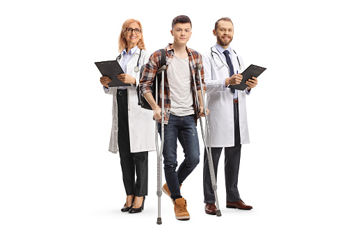 Team of doctors behind a male student with crutches isolated on white background