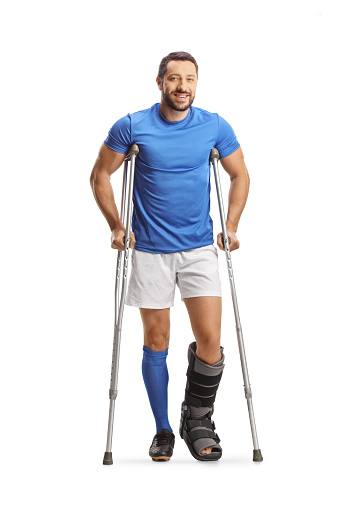 Full length portrait of a male athlete with crutches and a walking brace isolated on white background