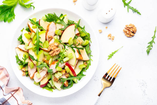 istock Waldorf salad with chicken fillet, red and green apples, raw celery, lettuce, arugula and walnuts on plate, white table background, top view 1496792025