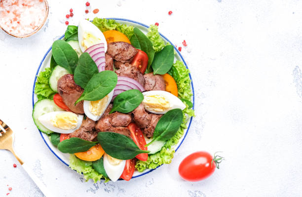 istock Perigord salad with roasted chicken liver, red tomatoes, cucumbers, boiled eggs, lettuce and spinach. Black kitchen table background, top view 1496792030