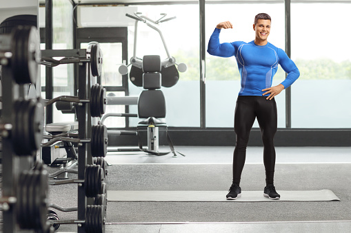 Full length portrait of a fit muscular man in leggings in a gym