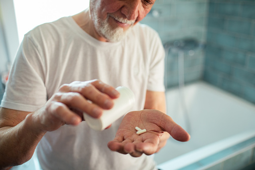 Close up of a senior man taking medicine in a bathroom