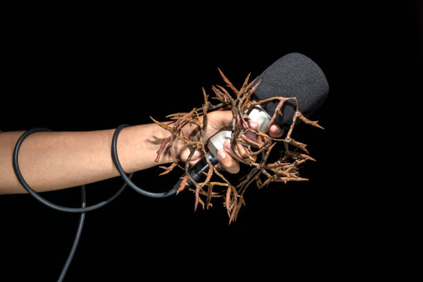 A human hand holding a microphone full of thorns with black background