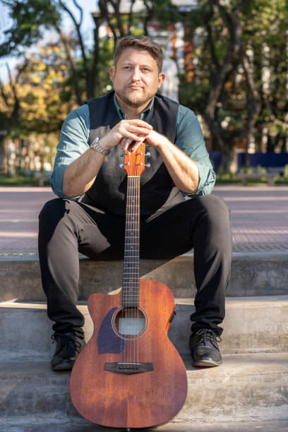 istock Guitarist sitting in a park posing with his guitar 1496807435