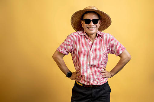 Man with a shirt wearing sunglasses and a hat standing on a colored background