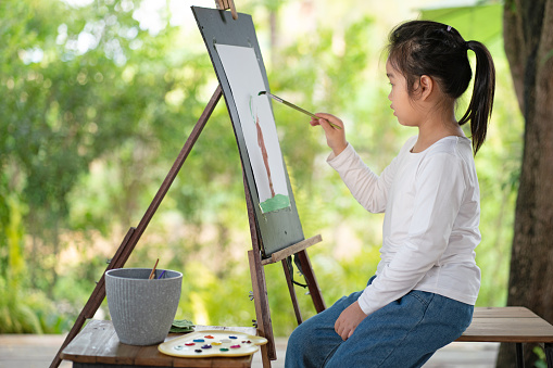 Little Asian girl doing leisure activities enjoying paint art work at the backyard