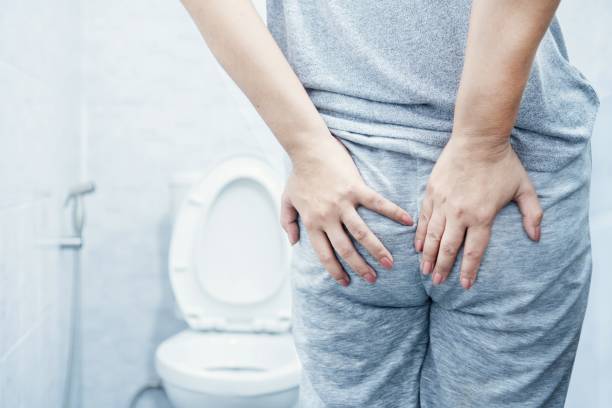 woman's hand holding butt due to hemorrhoid pain and discomfort in a toilet, chronic diarrhea stock photo