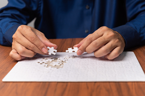 hands of businessmen joining white jigsaw pieces on table. Business concept.