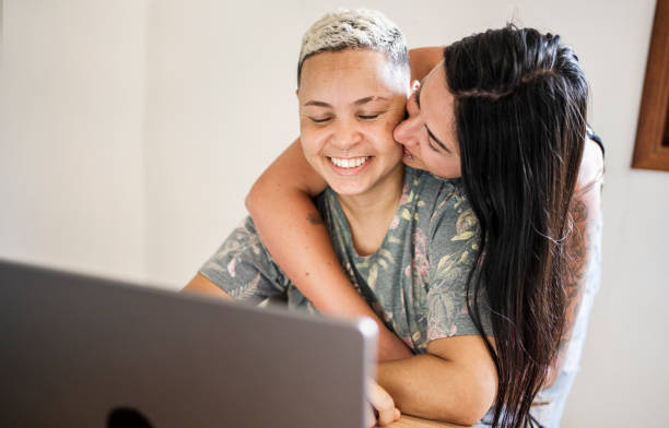 istock Happy woman using laptop with girlfriend hugging her at home 1496834782
