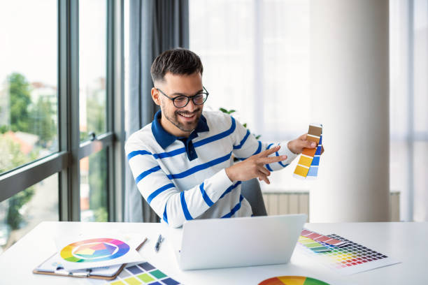 istock Cheerful man designer having video conference with clients, sitting at desk in front of computer, holding color palettes, gesturing and smiling, copy space 1496835036