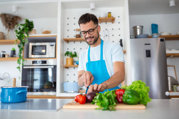 istock Handsome young man man stand at modern kitchen chop vegetables prepare fresh vegetable salad for dinner or lunch, young male cooking at home make breakfast follow healthy diet, vegetarian concept 1496835476