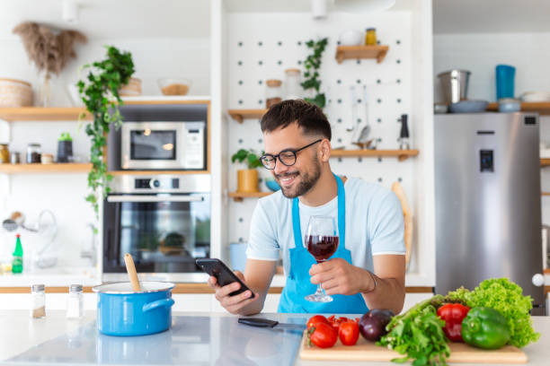 istock Happy young man preparing romantic dinner searching vegetable recipes diet menu cookbook app using smartphone, smiling husband holding phone cooking healthy vegan food cut salad in kitchen interior 1496835483