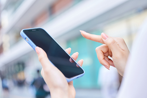 Hand of a woman using a smartphone on a street corner