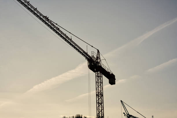 istock Industrial construction cranes and building silhouettes over sun at sunrise. 1496836670