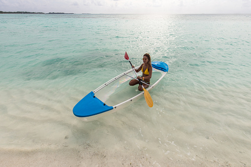 High angle view of young woman having fun while paddling a canoe in summer day at sea. Copy space.