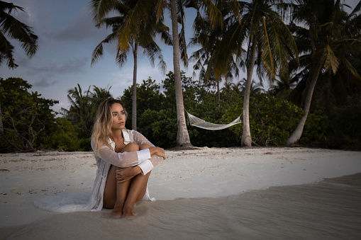 Young pensive woman relaxing in sand on the beach and looking away. Copy space.