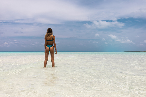 Back view of carefree woman standing in sea during summer day and looking at view. Copy space.