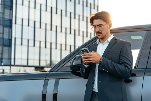 istock Young businessman standing near luxury car and using smartphone 1496844254
