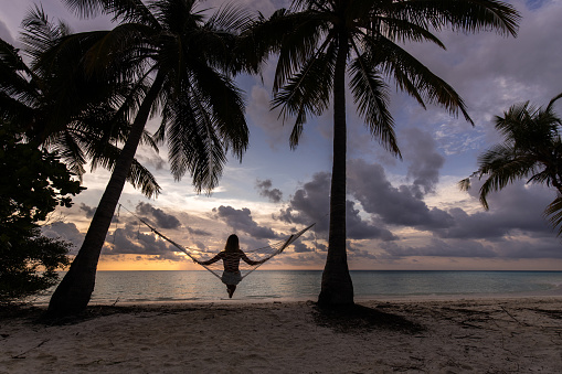Rear view of a relaxed woman looking at view from a hammock on the beach at sunset.