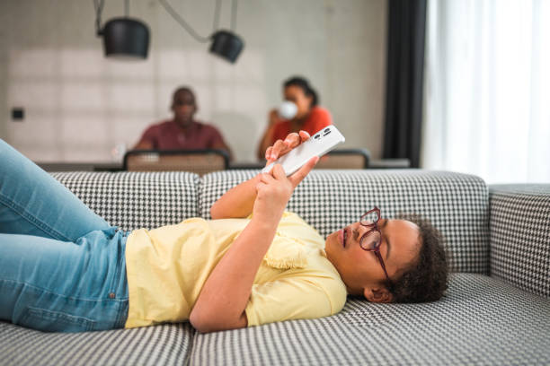 girl at home lying on the couch using smartphone - glasses child cute offspring imagens e fotografias de stock