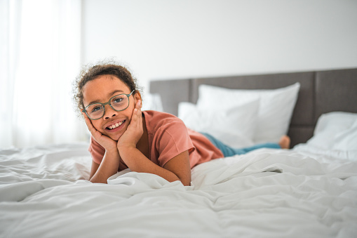 AA mixed race girl lying comfortably on a bed, looking at camera and wearing eyeglasses.