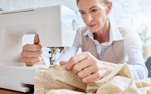 Tailor, senior woman and sewing machine for fabric clothes, luxury apparel or creative design in studio workshop atelier. Startup small business designer, service and sewer working on fashion outfit