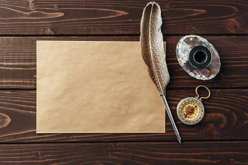 Top view photo of an old paper on brown wooden texture background with feather