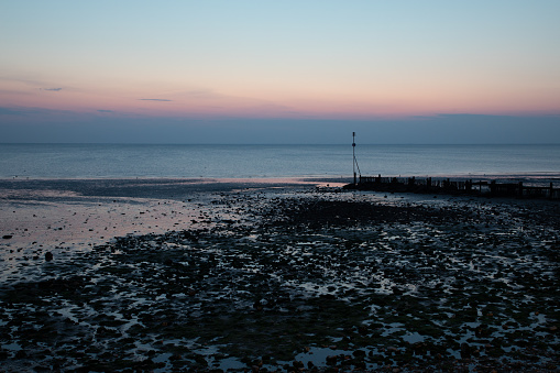 Sea groynes and reflected light over Hunstanton beach at sunset.