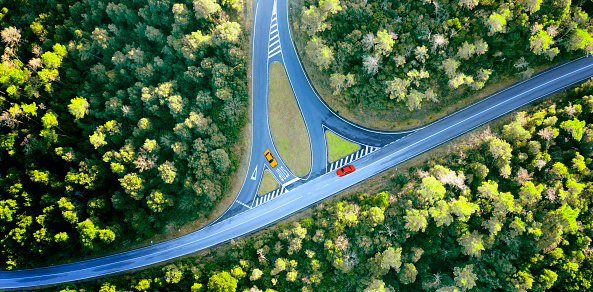 Aerial view of cars on road intersection through colorful autumn forest.